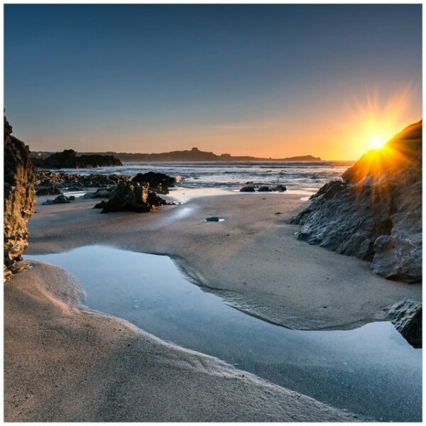 Wallario Möbelfolie Sonnenuntergang hinter einem Felsen am Strand